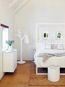 Double bed with white frame and clothes stand in shape of stylised tree in bright attic bedroom