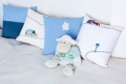 Soft toy sheep leaning against nursery cushions on white blanket