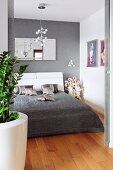 A double bed with a grey quilt and shimmering silver, decorative cushions in an elegant bedroom with pictures and a mirror on the wall