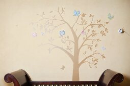 Baum mit Schmetterlingen als Wandbild hinter antikem Sitzmöbel aus Holz