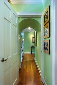 Blick durch geöffnete Tür in schmalen Flur mit grünen Wänden, Rundbogen & Holzboden