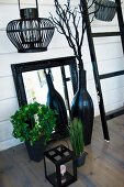 Black lantern, mirror with black-painted frame and black vase in front of white wooden wall
