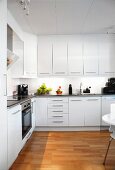 Spacious, white modern kitchen with corner counter, wall units and parquet flooring