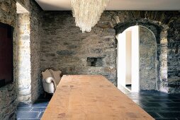 Chandelier above long table top and Baroque armchair against rustic stone walls in Ligurian farmhouse