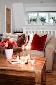 Beigefarbenes Polstersofa mit mehreren Kissen in gemütlichem Landhausambiente mit Kerzenlicht und rustikalem Couchtisch