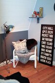Teenager's bedroom in grey and white with wooden floor, comfortable reading chair with sheepskins and black and white picture with lettering leaning on wall