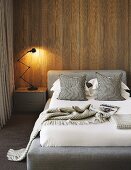 Classic table lamp on bedside cabinet next to bed with upholstered headboard against wood-clad wall