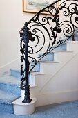 Treppenaufgang mit blauem Hochflorteppich und schmiedeeisernem Handlauf mit floralen Motiven