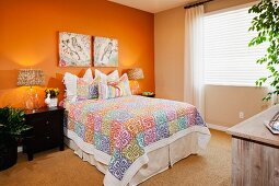 Bett mit bunter Tagesdecke in Schlafzimmer mit orangefarbener Wand