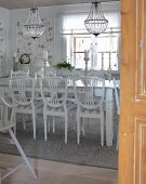 Blick durch offene Tür in Esszimmer mit weissen Holzstühlen um Tisch, darüber Kronleuchter mit Glasschmuck