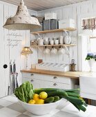 Blick über Schale mit Zitronen und Gemüse auf Küchenzeile, darüber an Wand aufgehängte Konsolen mit weißem Geschirr