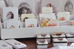 Rose-patterned, china boxes in front of white wooden rack of vintage gift tags