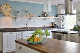 Landhausküche mit weissen Unterschränken, im Hintergrund Küchenzeile vor gefliestem Spritzschutz in Weiß, oberhalb hellblau getönte Wand