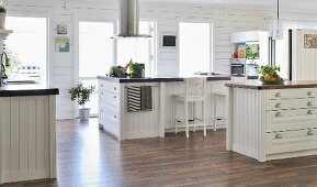Spacious, white, country-house-style kitchen with free-standing island counter under stainless steel extractor hood