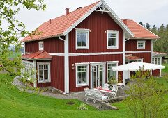 Falu red and white Swedish wooden house with terrace situated in lush, green landscape