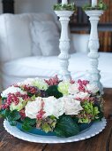 Wreath of white roses and berries on table in front of white ceramic candlesticks