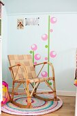 Rocking chair with woven textile seat on colourful crocheted rug and wall sticker motif in child's bedroom