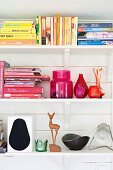 Books arranged by colour, vases and stylised deer ornament on white shelves
