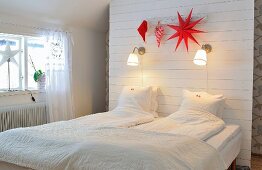 Attic bedroom with storage space behind partition headboard and reading lamps and red Christmas decorations above bed