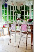 Thonet chairs with white, peeling paint around table in conservatory with floor-to-ceiling lattice windows
