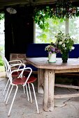 White, delicate metal chairs at rustic wooden table with vases of flowers on stone loggia floor