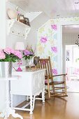 Wooden rocking chair next to flowers on white, ornate cabinet