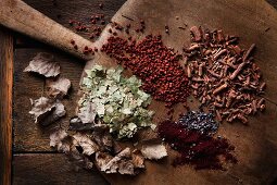 Verschiedene Rohstoffe zum Färben von Eiern auf altem Holzbrett: getrocknete Birkenblätter, echtes Karminrot, rötliche Körner