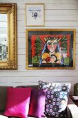Modern artwork and gold-framed mirror on wood-panelled wall - floral and plain scatter cushions on sofa