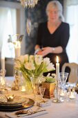Festively set table with flower arrangement, candlelight and woman in background