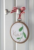 'Kiss' and mistletoe embroidered on fabric in embroidery hoop frame hung from door knob