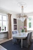 Stühle mit grauen Hussen um klassizistischen Esstisch, unter Kronleuchter mit Stuckelement an Decke in traditionellem Esszimmer