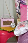 Pink retro radio and alarm clock on pink vintage stool and bed linen with large floral pattern