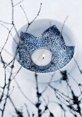 Tealight and blue fabric star with silver glitter in china bowl on snowy ground