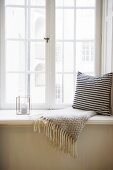 Cushion with black and white cover and fringed blanket next to candle lantern on window sill