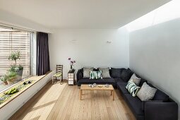 Eckcouch mit grauem Stoffbezug in minimalistischer Wohnraum mit Dielenboden und Panoramafenster mit eingebauter Bank