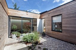 Planters on pebble area and wooden deck in courtyard of contemporary house with wood-clad facade