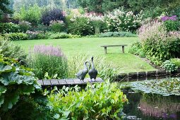 Gänsefiguren auf Holzsteg am Teich im elegant angelegten Garten