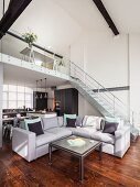 Coffee table and grey corner sofa in open-plan, loft-style interior with staircase leading to gallery in background