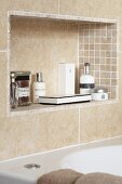Sand-coloured tiles on wall and in niche with toiletries above bathtub