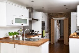 Modern, white fitted kitchens with wooden work surfaces; open double doors in brick wall in background