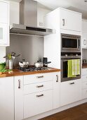 Gas hob with extractor hood and separate oven and microwave in white, fitted kitchen with wooden work surfaces