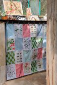 Patchwork curtain made from fabric remnants with colourful patterns and old prints of plants and butterflies hiding shelves of utensils in greenhouse
