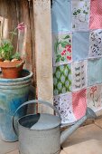 Patchwork curtain made from fabric remnants with colourful patterns and vintage prints of plants and butterflies; watering can in foreground