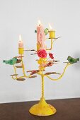Brennende Kerzen auf gelb lackiertem, romantischem Kerzenhalter mit Vogelfiguren und Blumenmotiven dekoriert