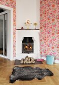 Animal-skin rug in front of fire in corner stove and pink, floral wallpaper in country-house interior