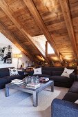 Sofa set and coffee table under sloping, rustic, wood-panelled ceiling