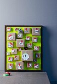 Hand-crafted Advent calendar with small parcels attached to picture frame with green background leaning against wall