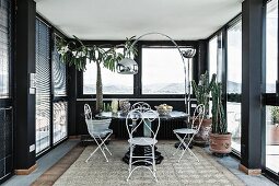 Seating area with delicate, white metal chairs and arc lamp in black conservatory of penthouse apartment
