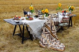 Gedeckter Tisch im Stoppelfeld mit weisser Leinentischdecke und goldgelben Sonnenblumen