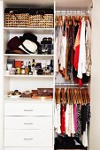 Fashion accessories on shelves and clothing on coat hangers in fitted wardrobe with open door